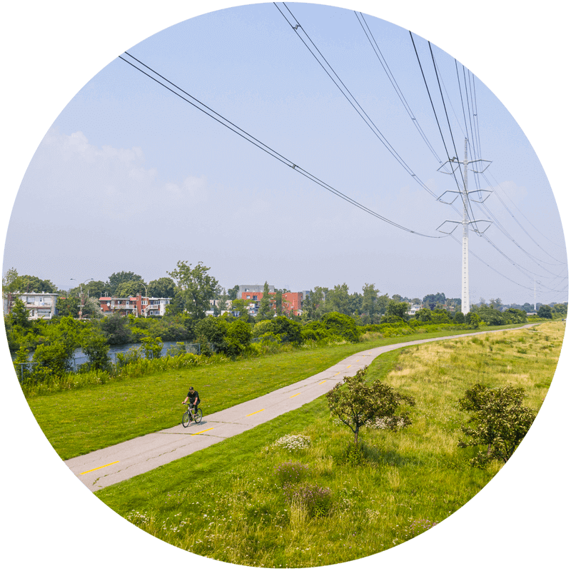 Individus qui circulent à vélo sur une piste cyclable située sous les fils électriques et près d’un quartier résidentiel.
